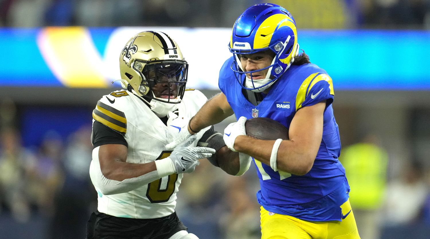 Puka Nacua runs with the ball in one hand as he reaches behind him to block a Saints player chasing him